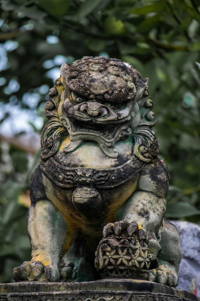 Detailed shot of an ancient stone lion statue surrounded by greenery.